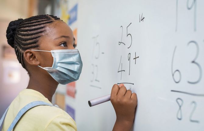 Portrait of girl wearing face mask and writing solution of sums on white board at school. Credit: Rido via Shutterstock Portrait of girl wearing face mask and writing solution of sums on white board at school. Credit: Rido via Shutterstock